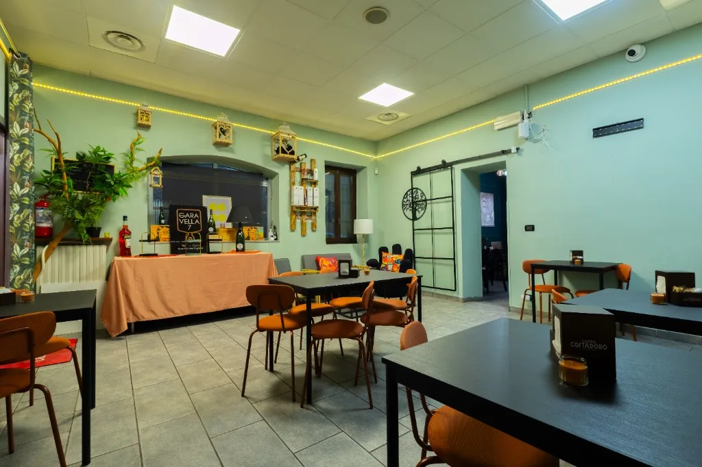 Sala con pareti menta, tavoli neri e sedie arancioni